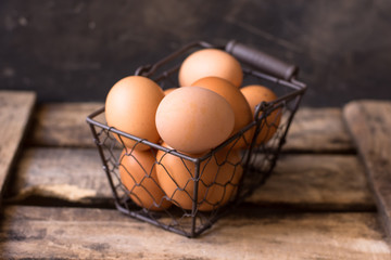 Fresh brown eggs in a wire basket on a vintage wood box, black background, Easter, decoration, rural rustic einterior, farming concept