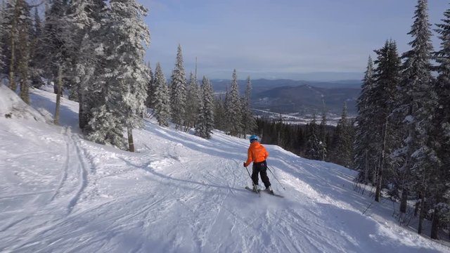 Skier is riding down fast upon narrow ski track on the background of winter mountains
