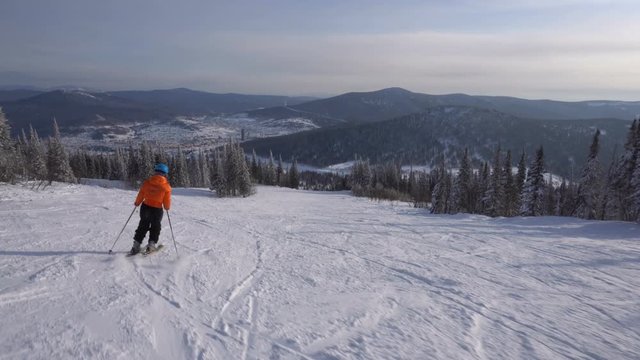 Skier is riding down fast upon ski track on the background of winter mountains