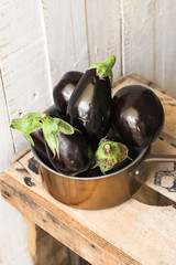Purple mini eggplants in a copper dipper on vintage wood box on white background,top view, rustic rural style,summer fall, autumn harvest