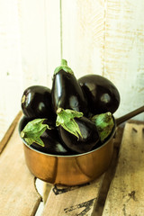 Purple mini eggplants in a copper dipper on vintage wood box on white background,top angle view, rustic rural style,summer fall, autumn harvest