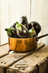 Purple mini eggplants in a copper dipper on vintage wood box on white background,selective focus, rustic rural style,summer fall, autumn harvest,mediterranean cuisine