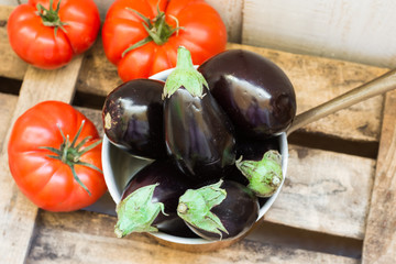 Mini eggplants in copper dipper and ripe raff tomatoes on weathered wood box,top view,rural rustic style,summer fall harvest