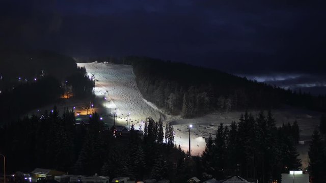 Night skiing and snowboarding at a ski resort and running ski lifts.
