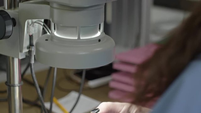 Tilt up of woman inspecting printed circuit board assembly with microscope in laboratory