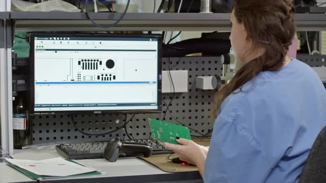 Rear view of woman scanning printed circuit board assembly and working on computer 