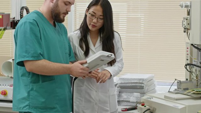 Technician and young Asian woman in lab coat using device to operate metal etching scriber