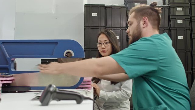 Technician separating PCB material with cutting machine while working with female assistant 