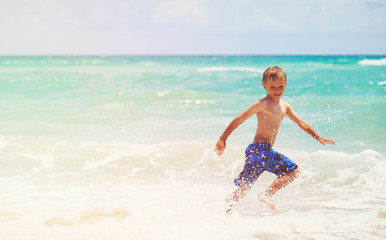 Fototapeta premium happy little boy run play with waves on beach