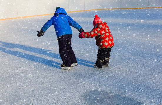 little brother teaching sister to skate in winter snow