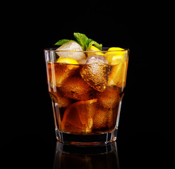Glass of cola with ice, mint and lemon on black background