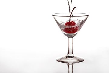 Pour sparkling water or soda into a glass with a cherry on white background