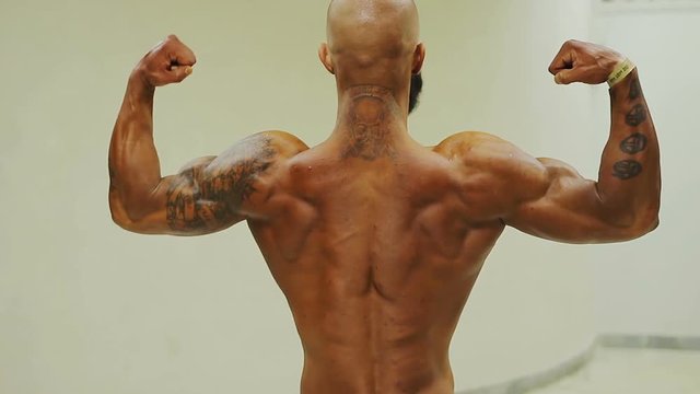 Strong tanned bodybuilder demonstrating rear double bicep pose, muscular man