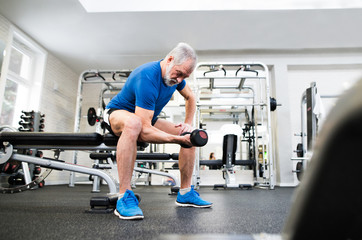 Obraz na płótnie Canvas Senior man in gym working out with weights.