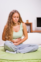 Fototapeta premium Young woman is sitting in her bed with stomachache.