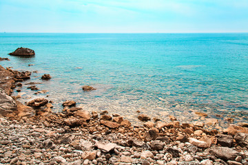 Rocky shore of blue sea on sunny day. Seascape, mediterranean coastline and stones. Natural background.