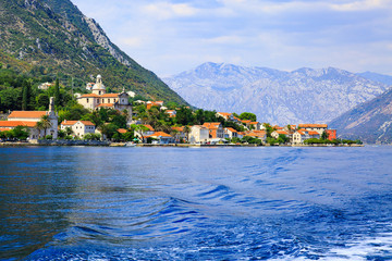 Waterfront of small town Prcanj along Bay of Kotor, Montenegro. View of Birth of Our Lady Church, coastal villas, gardens and mountain from sea.