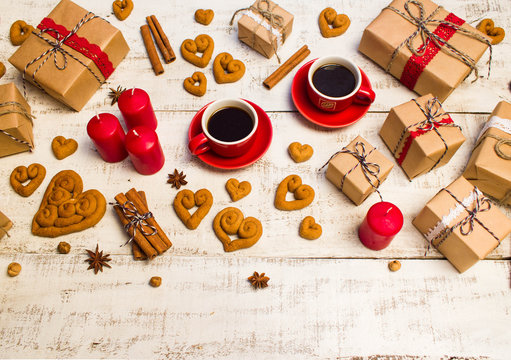 Two red coffee cups, gifts, cookies in the shape of a heart   on a white wooden background