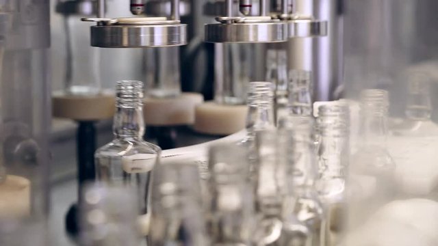 Spill of alcohol in glass bottles at the plant. Conveyor belt with glass bottles. Shop the spillage of alcoholic beverages. Conveyor close-up. The production process of alcoholic beverages. 4K res.