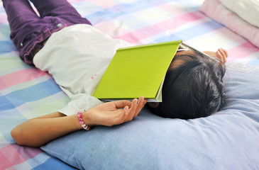 asian child sleeping on book with a book covering her face