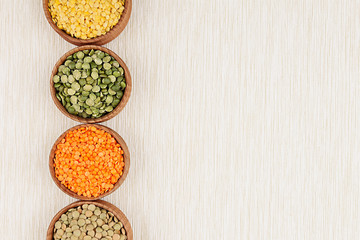 Assortment of lentils in a wooden bowls with copy space on white fabric background. Top view, closeup. Healthy protein food.