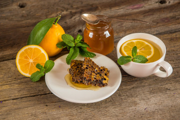 Honeycomb, honey in jar, green tea, lemon with leaf and mint on