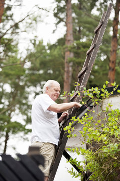 Senior man on ladder clearing drainpipe