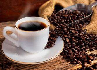 Hot coffee with cup and coffee bean bag on old wood background
