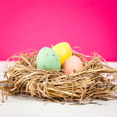 tre pastellfärgade ägg i fågelbo på rosa bakgrund