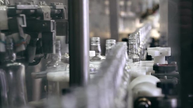 Spill of alcohol in glass bottles at the plant. Conveyor belt with glass bottles. Shop the spillage of alcoholic beverages. Conveyor close-up. The production process of alcoholic beverages. 4K res.