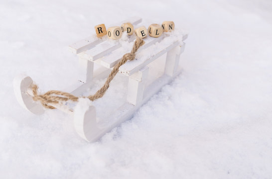 Weißer Holzschlitten im Schnee mit dem Wort Rodeln in Buchstabenwürfeln
