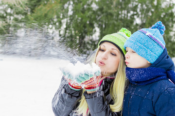 Happy little cute baby and mother on a sunny winter day playing with the snow  blowing  