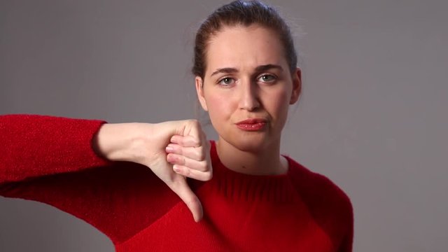 annoyed young woman sulking, expressing her disagreement with thumbs down