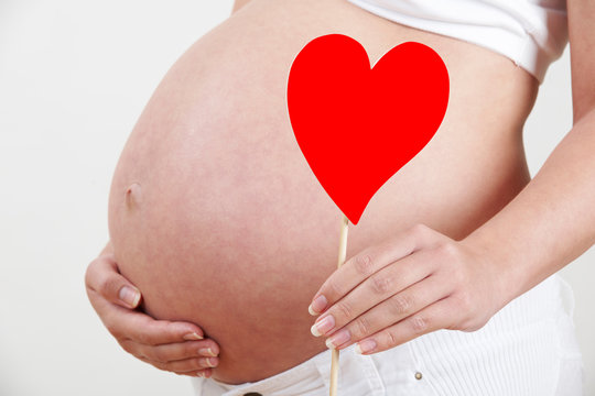 Close Up Of Pregnant Woman Holding Heart Shape On Stick