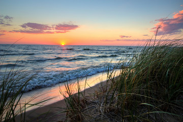 Tranquil Sunset Beach Background.  Beautiful sunset horizon over water with a sandy beach and dune grass in the foreground. Hoffmaster State Park. Muskegon, Michigan