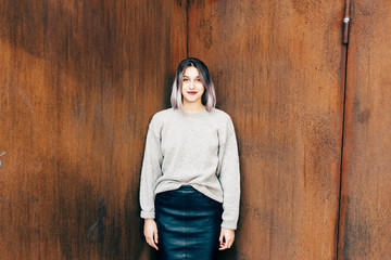 Young beautiful caucasian purple grey hair woman outdoor in the city leaning on colorful wall, looking at camera, smiling - happiness, carefree, serene concept