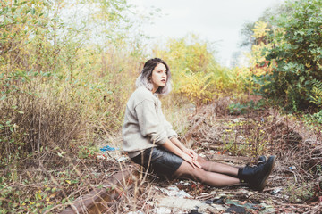 Young beautiful caucasian purple grey hair woman outdoor in the city sitting on abandoned railway, looking over - serious, pensive, thinking future concept