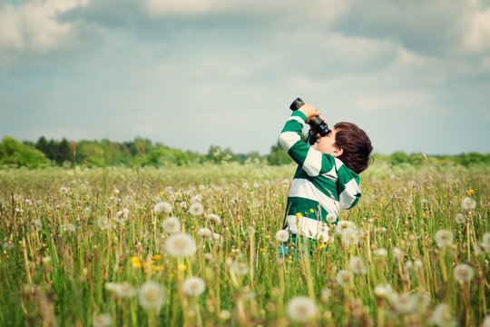 Child wathing in benoculars on the field with dandelions. Boy playing on the meadow in summer