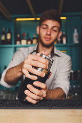 Young handsome barman in bar shaking and mixing alcohol cocktail