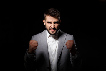 Obraz premium Rage young successful businessman angering over black background.