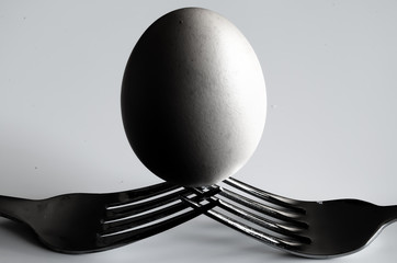 single egg balanced on two forks in black and white