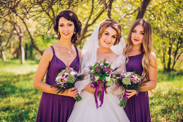 Bride with bridesmaids outdoors in sunny green garden on the wedding day