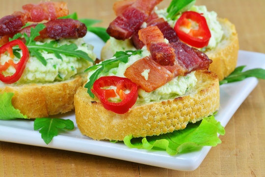 Canapes with herbed cream cheese, bacon, chilly and rucola on white plate