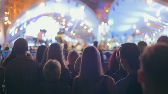 Silhouettes of crowd in beams of colorful light on concert at night