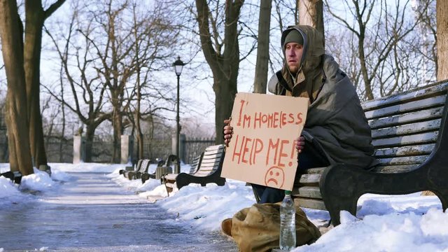 
4K.Homeless young man with cardboard in  winter city park
