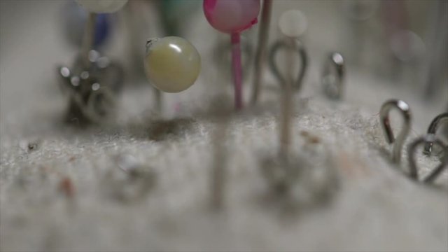 Various colorful needles and pins in a grey pincushion macro closeup