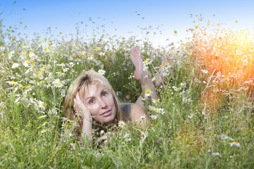 The beautiful happy young woman lies in the field of camomiles