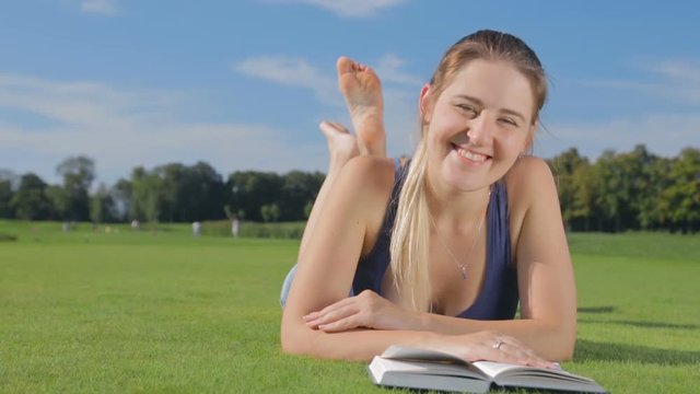 Dolly shot of smiling young girl lying on grass at park with a book
