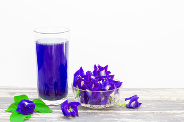 Flower butterfly pea juice in glass with fresh flowers and green leaves on vintage wooden table on white background, health care concept