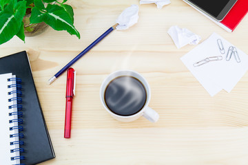 Hot coffee cup with smartphone, glasses, notebooks, pen, pencil, paper clips, green leaves pot on vintage wooden table